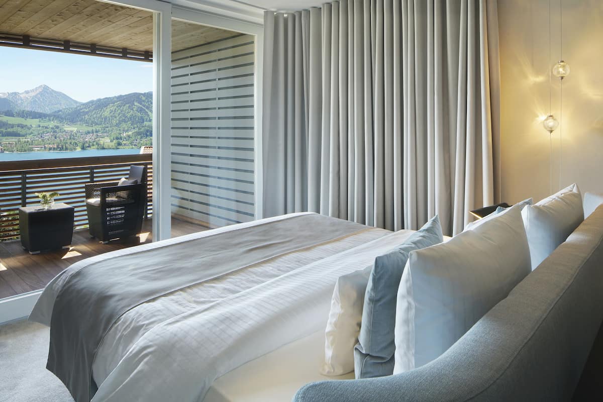 A bedroom with a large bed, a balcony with a view of mountains, and a sliding glass door.
