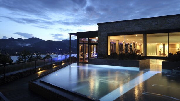 A modern building with a glass facade, a rooftop infinity pool, and a view of mountains and a body of water. - Das Tegernsee (Tegernsee)