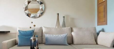 Un salon moderne avec un canapé d’angle, un grand miroir rond et des vases décoratifs.