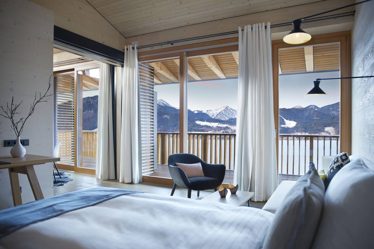 A bedroom with a bed, a chair, a table, and a view of mountains.