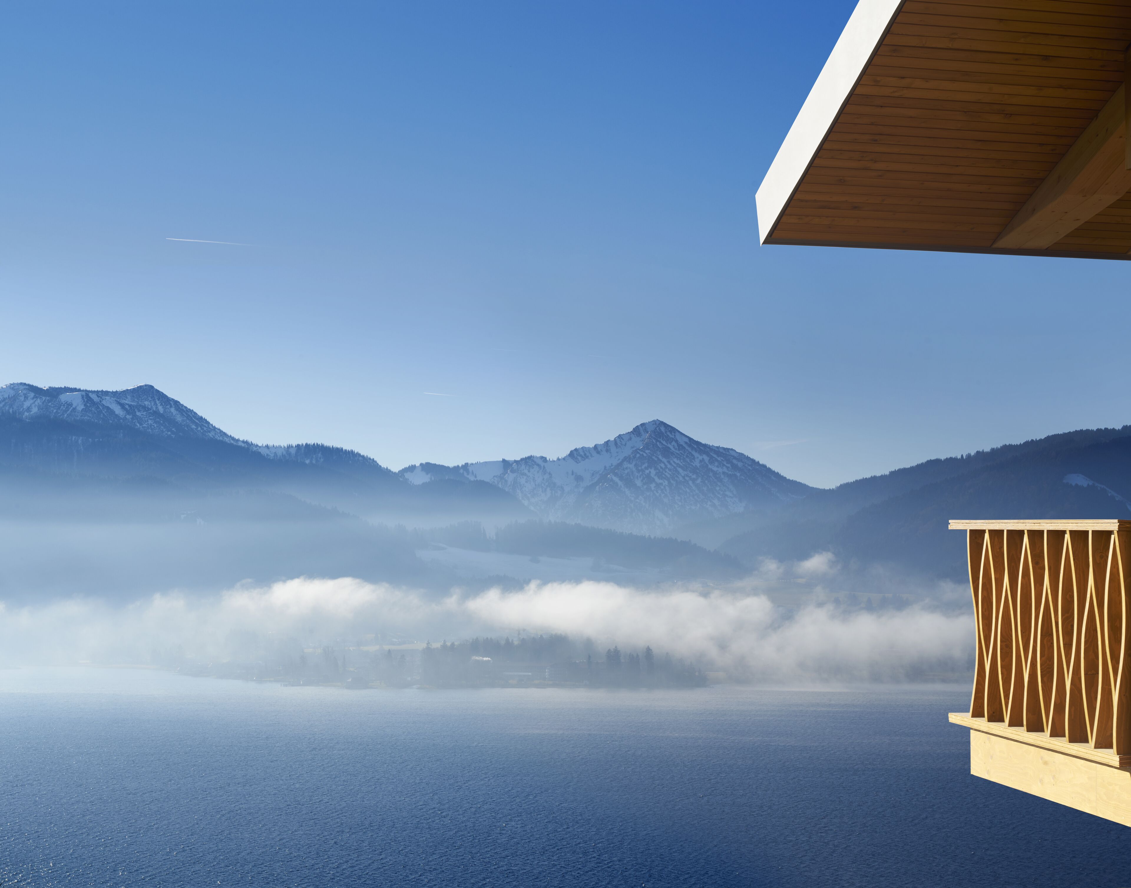 A view of a mountainous landscape with a body of water in the foreground, a wooden structure with a sloped roof, and a clear sky.