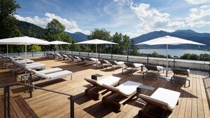 A wooden deck with sun loungers and umbrellas overlooking a lake and mountains. - Das Tegernsee (Tegernsee)