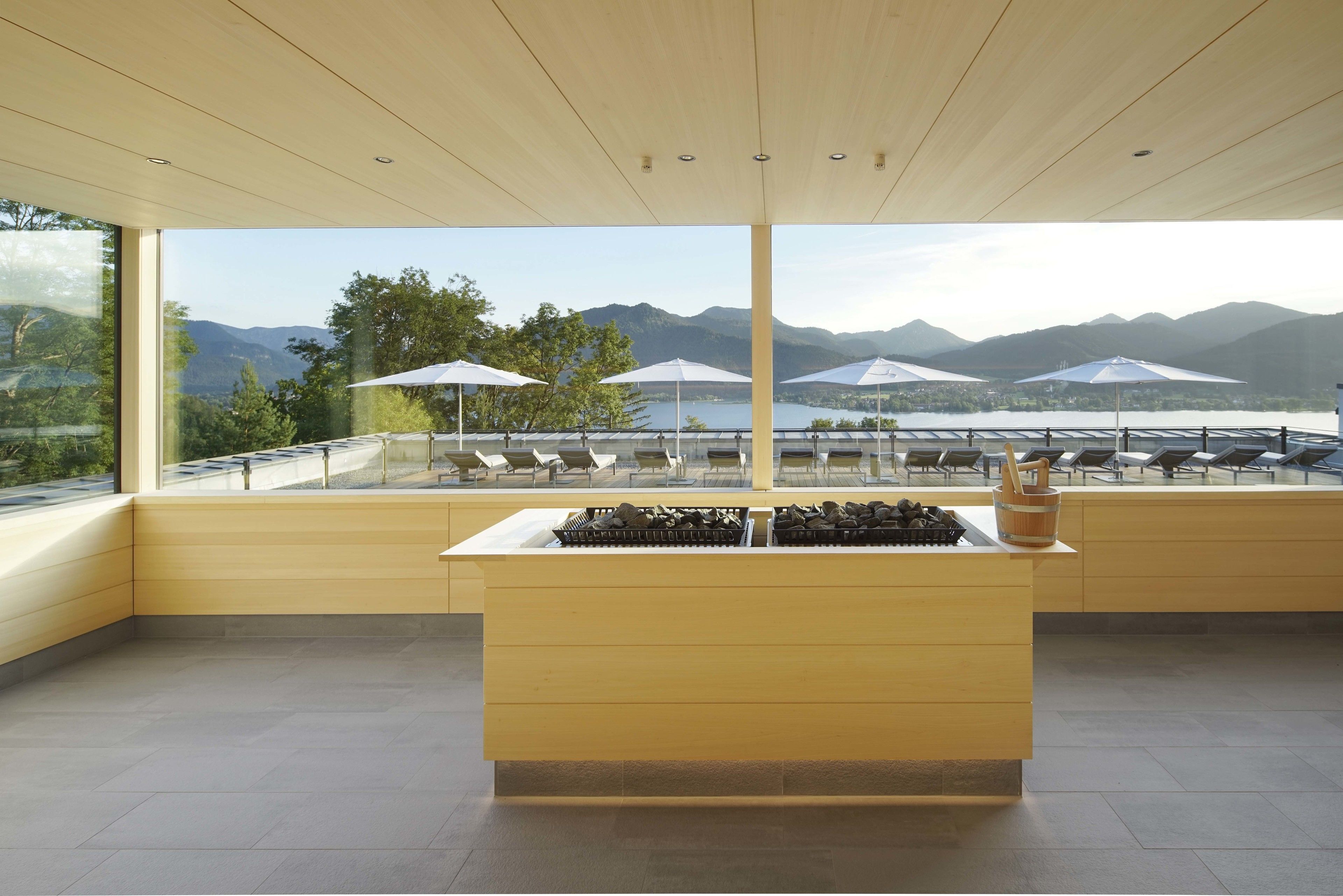 Un intérieur moderne avec un îlot central, un espace salon agrémenté de parasols et une vue sur les montagnes et l’eau.