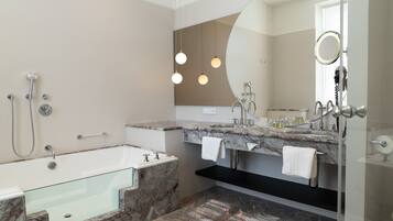 A modern bathroom with a glass-enclosed bathtub, a vanity with a marble countertop, and a large mirror with a round frame.