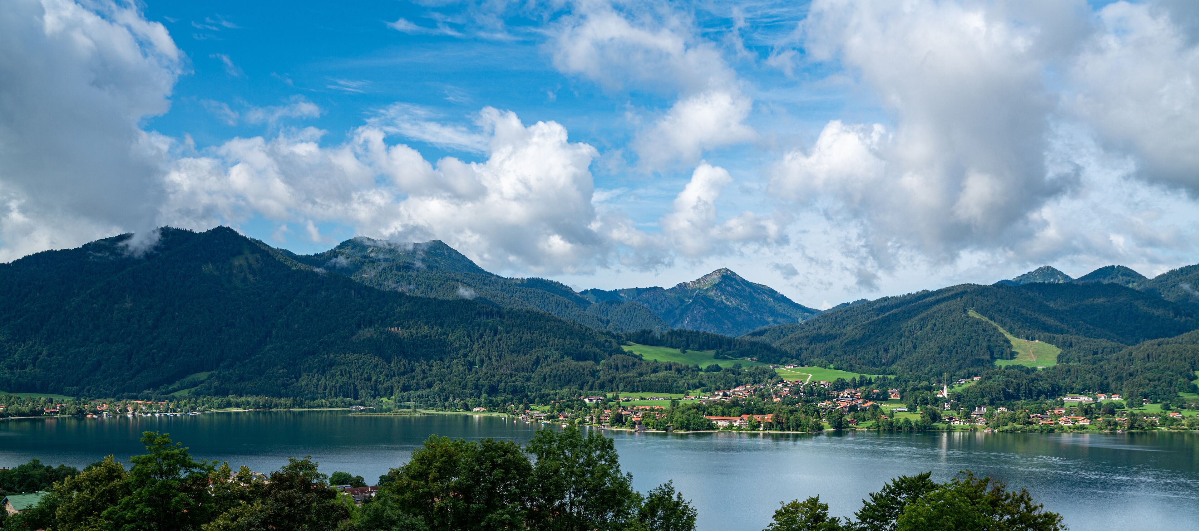 Um lago rodeado por montanhas, uma pequena cidade e o campanário de uma igreja.
