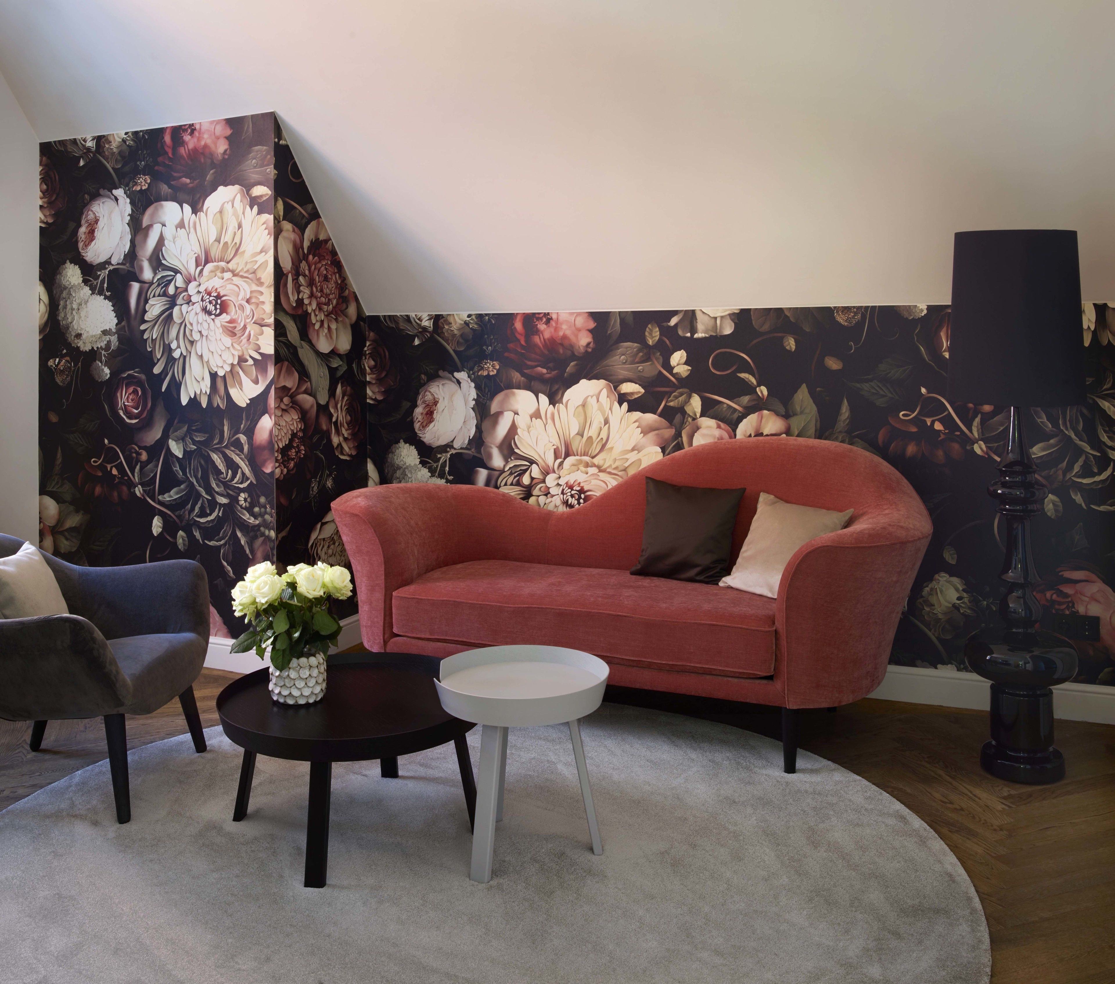 Un salón con un sofá rojo, un sillón gris, una mesa de centro redonda y una lámpara de pie negra.
