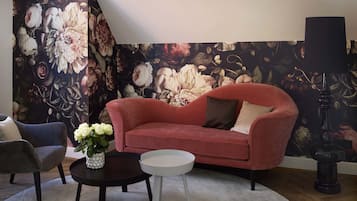Ein Wohnzimmer mit einem roten Sofa, einem grauen Sessel, einem runden Couchtisch und einer schwarzen Stehlampe.