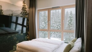 Une chambre à coucher avec un lit, une fenêtre donnant sur des arbres couverts de neige et un téléviseur fixé au mur.