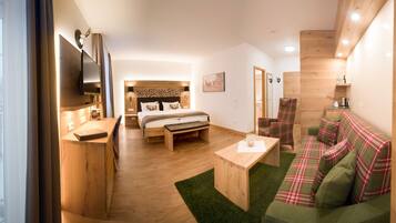 A modern hotel room with a wooden floor, a bed with a headboard, a green sofa, a wooden coffee table, and a TV mounted on the wall.