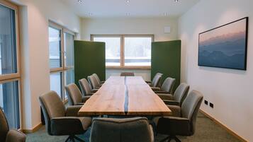 A conference room with a long table, chairs, large windows, and a framed picture on the wall.