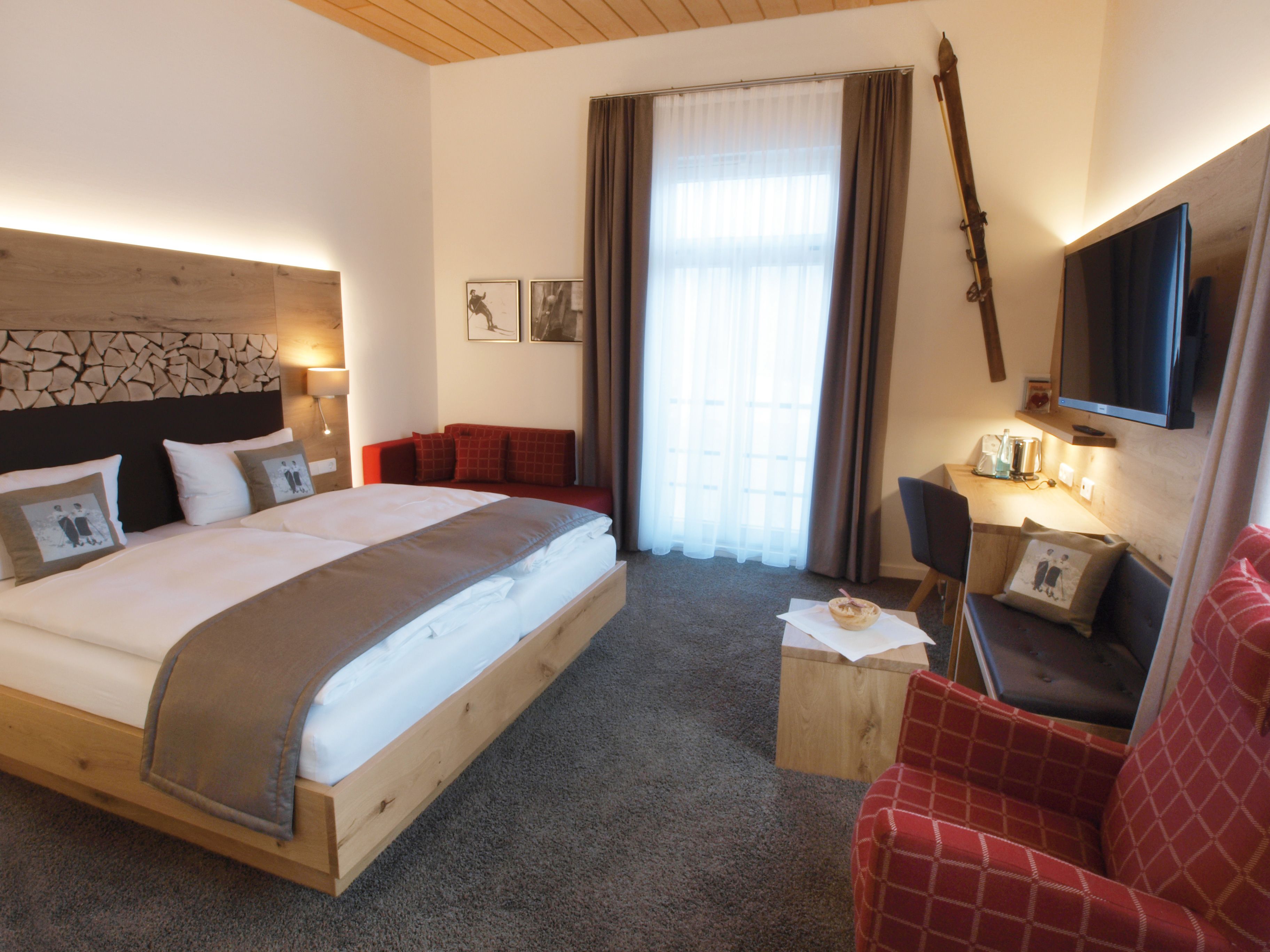 A hotel room with a large bed, a desk, a chair, a TV, and a window with curtains.