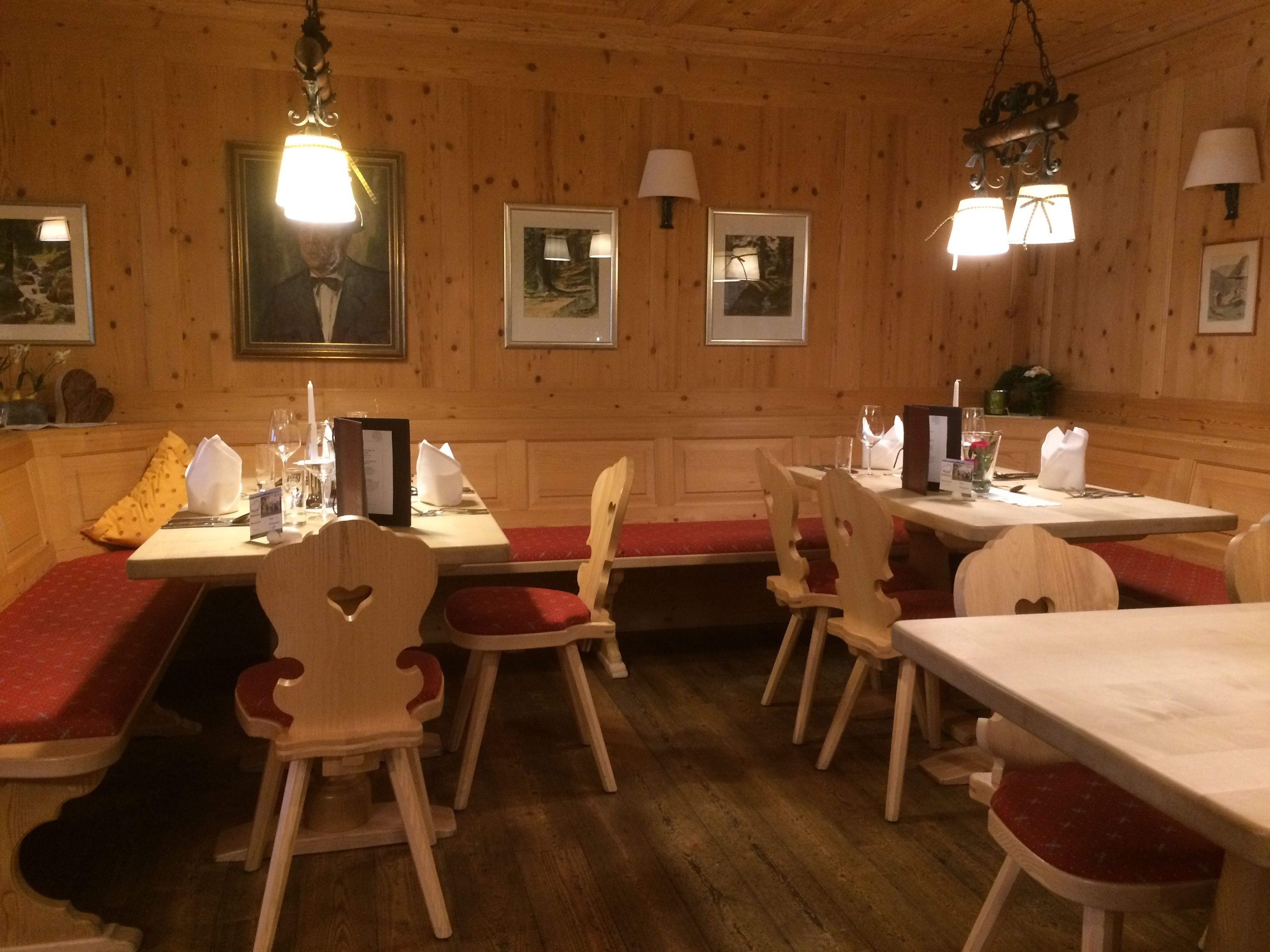 Ein Essbereich mit Holzwandverkleidung, Holzstühlen und -bänken, Tischen mit weißen Tischdecken und gerahmten Bildern an den Wänden.