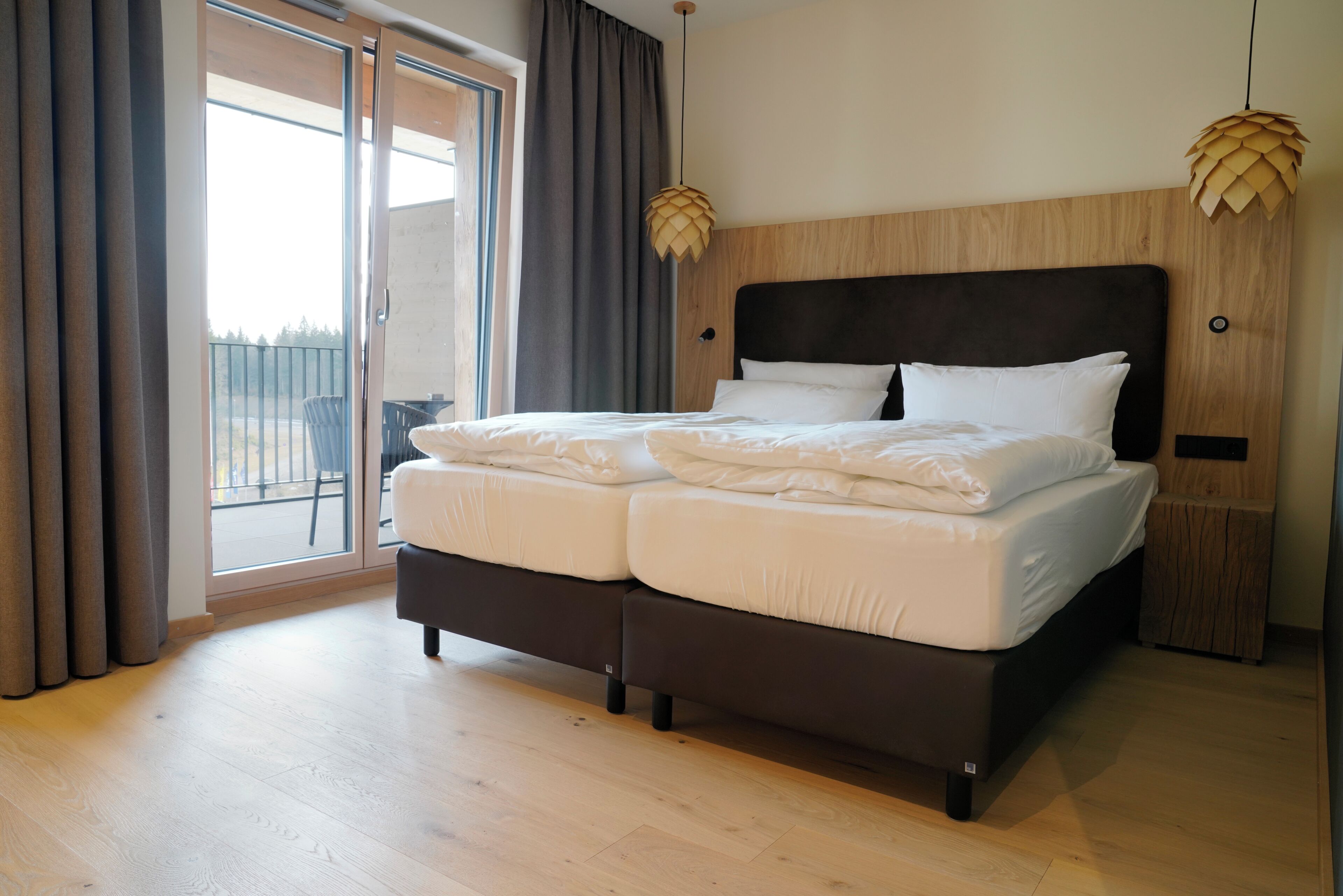 Ein Schlafzimmer mit einem großen Bett, einem Holzkopfteil, einer Glastür zum Balkon und zwei Pendelleuchten.
