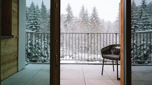 Een balkon met een stoel, uitzicht op besneeuwde bomen en een houten muur.
