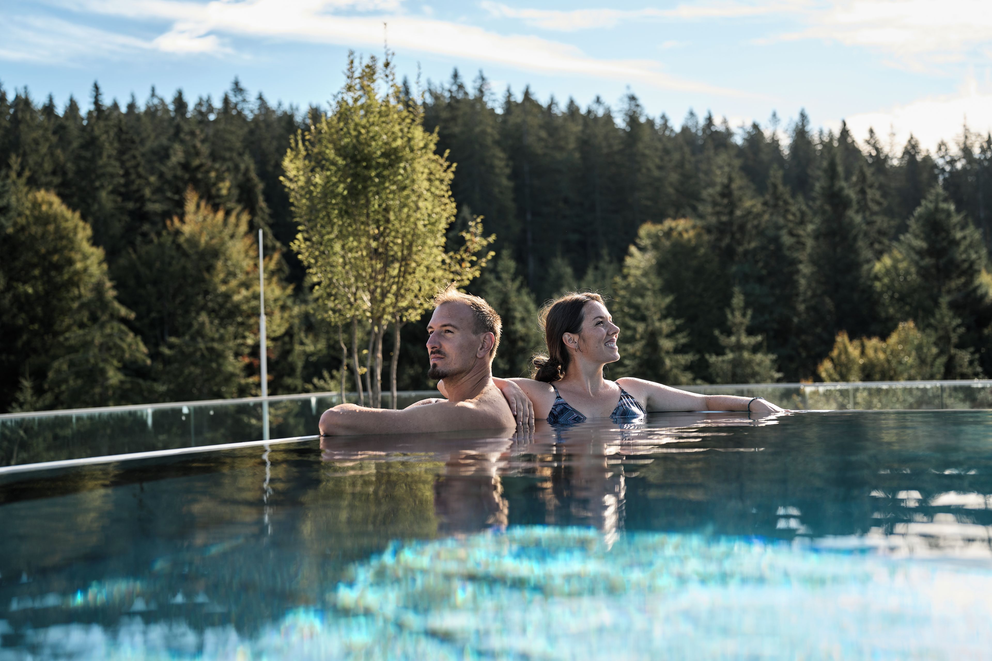 Piscina com água cristalina, cercada por árvores e um muro.
