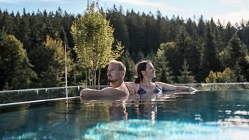 Piscina com água cristalina, cercada por árvores e um muro.