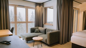 Une chambre moderne avec un canapé, une table ronde, un lit et de grandes fenêtres équipées de rideaux.