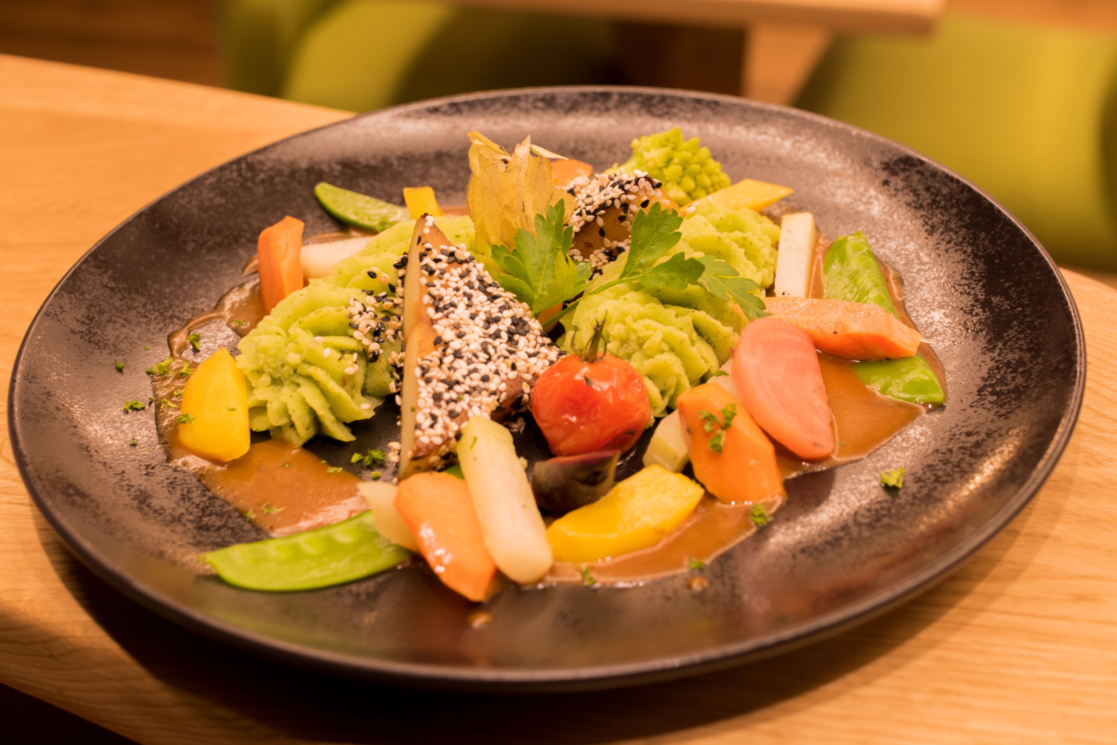 A plate of colorful vegetables and tofu on a dark plate.