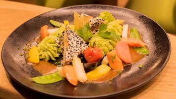 A plate of colorful vegetables and tofu on a dark plate.