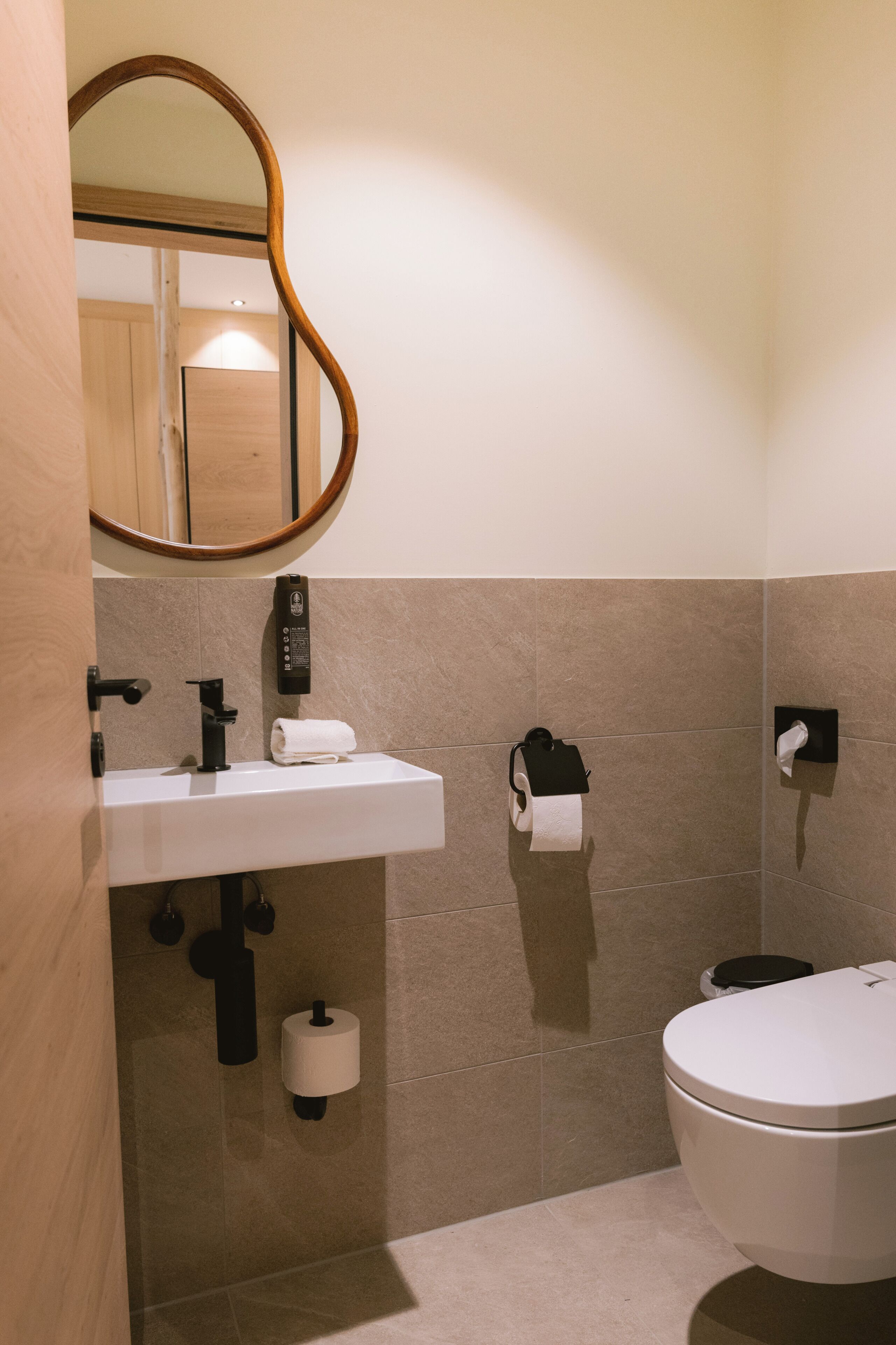 Un baño con lavamanos blanco, inodoro, espejo y dispensador de toallas.