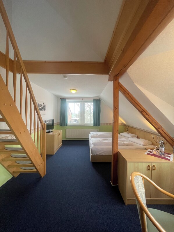 A bedroom with a wooden staircase, a bed, a desk, and a window with curtains.