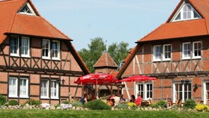 A traditional half-timbered building with a central tower, red umbrellas, and a well-maintained garden. - Flair Seehotel Zielow (Südmüritz)