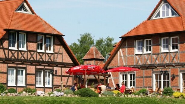 Un bâtiment traditionnel à colombages, doté d’une tour centrale, de parasols rouges et d’un jardin bien entretenu.