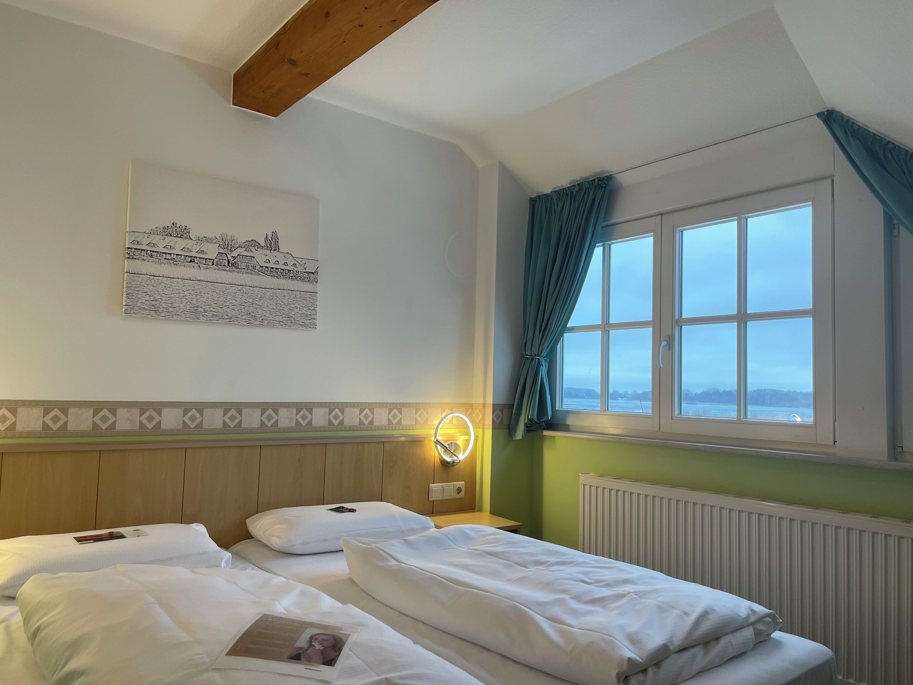 A hotel room with two beds, a window with curtains, a radiator, and a wall-mounted light.