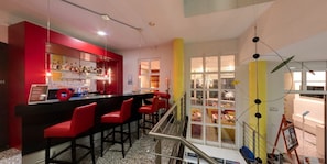 A bar area with red chairs and a bar counter, a staircase with a railing, and a view of the outdoor area through large windows.