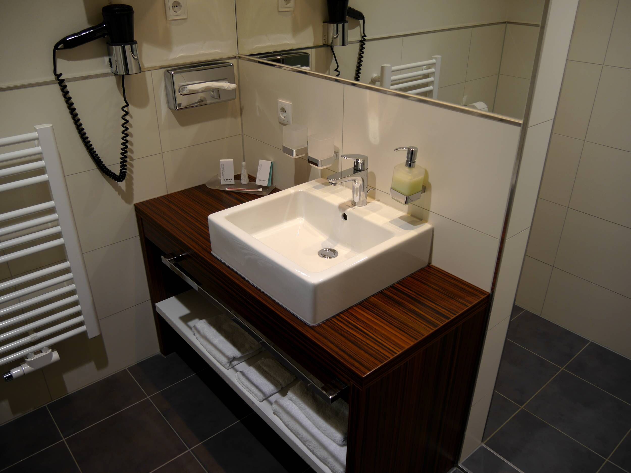 Ein Badezimmer mit weißem Waschbecken, Holzschrank, Handtuchhalter und Spiegel.