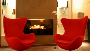A modern living room with two red chairs, a fireplace, and a bookshelf. - Business - Hotel Artes (Chemnitz)