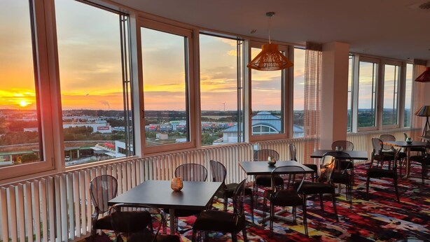 A dining area with large windows, a patterned carpet, and a hanging light fixture. - Business - Hotel Artes (Chemnitz)