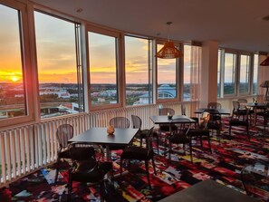 A dining area with large windows, a patterned carpet, and a hanging light fixture. - Business - Hotel Artes (Chemnitz)