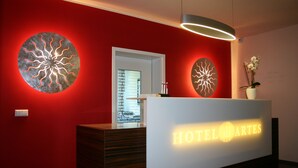 A hotel reception desk with a red wall and modern decor, including circular light fixtures and a welcome sign. - Business - Hotel Artes (Chemnitz)