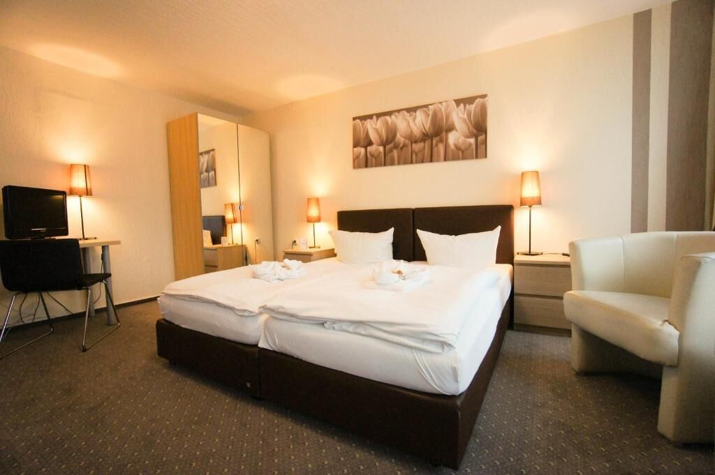 A hotel room with a large bed, two bedside tables with lamps, a desk with a chair, a TV, and a mirror.