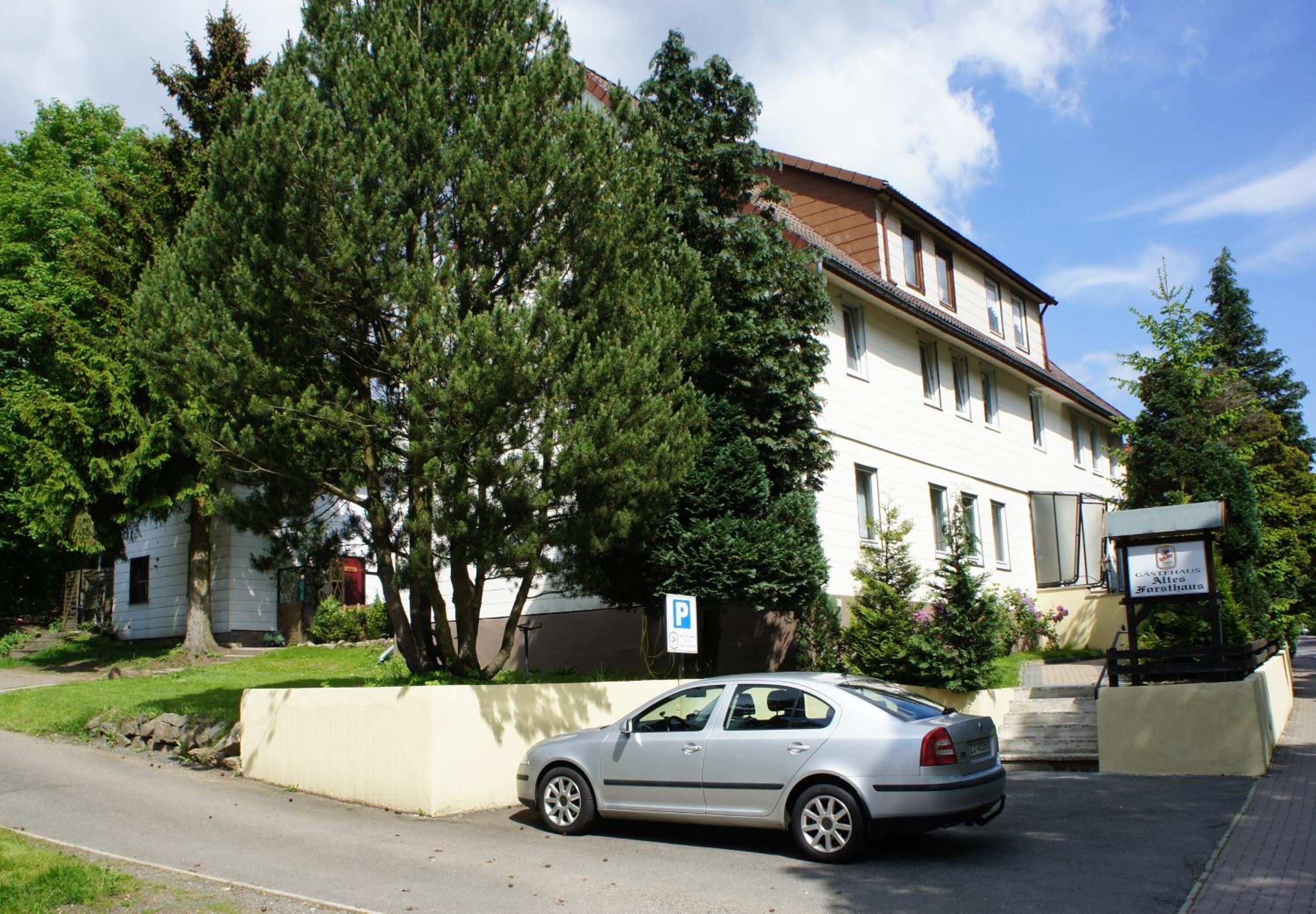 A silver car parked in front of a building with a parking sign.