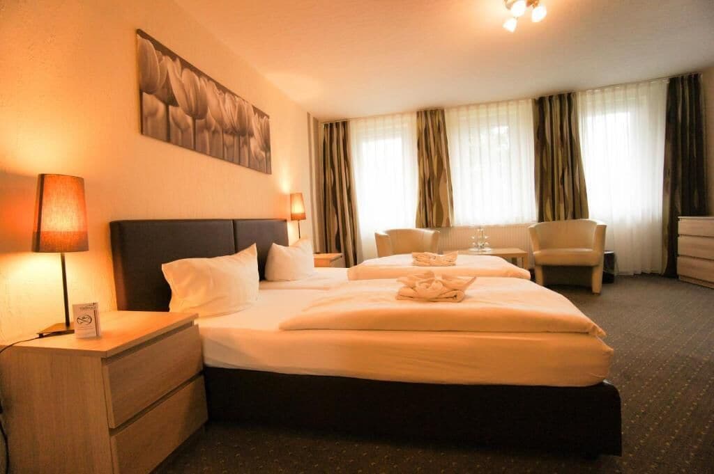 Ein Hotelzimmer mit einem großen Bett, einem Nachttisch mit Lampe, einem Sessel und einem Bild an der Wand.