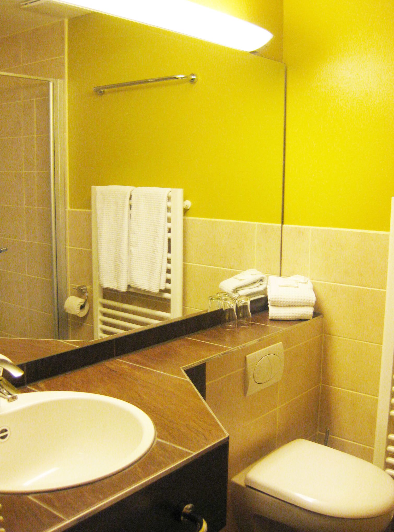 Ein Badezimmer mit weißem Waschbecken, einem Spiegel, einem Handtuchhalter mit gefalteten Handtüchern und einer Toilette.