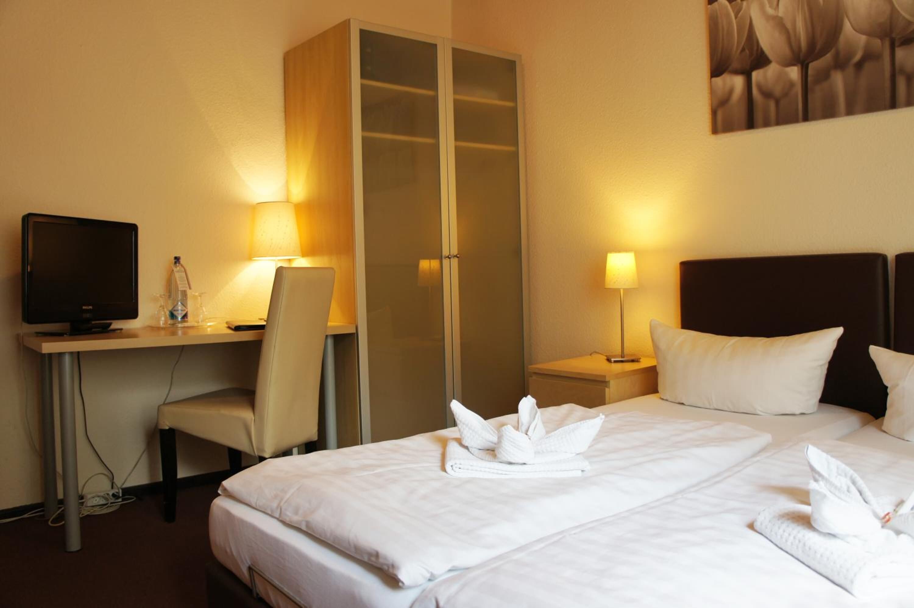 Una habitación de hotel con una cama, un escritorio con computadora, una silla y un armario.