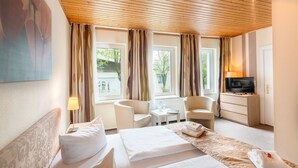 Quarto de hotel com cama, duas cadeiras, televisão e janela com cortinas.
