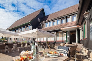 An outdoor dining area with wicker chairs and tables, a bottle of water, and a plate of food. - Altes Forsthaus Braunlage (Braunlage)