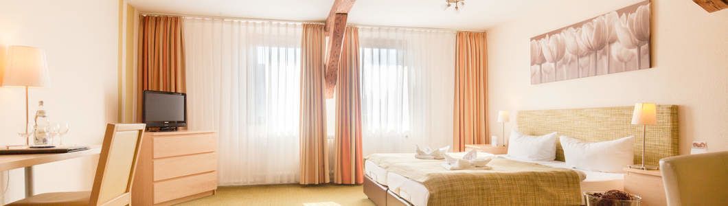 A hotel room with a bed, a television, a desk with a lamp, and a painting on the wall.