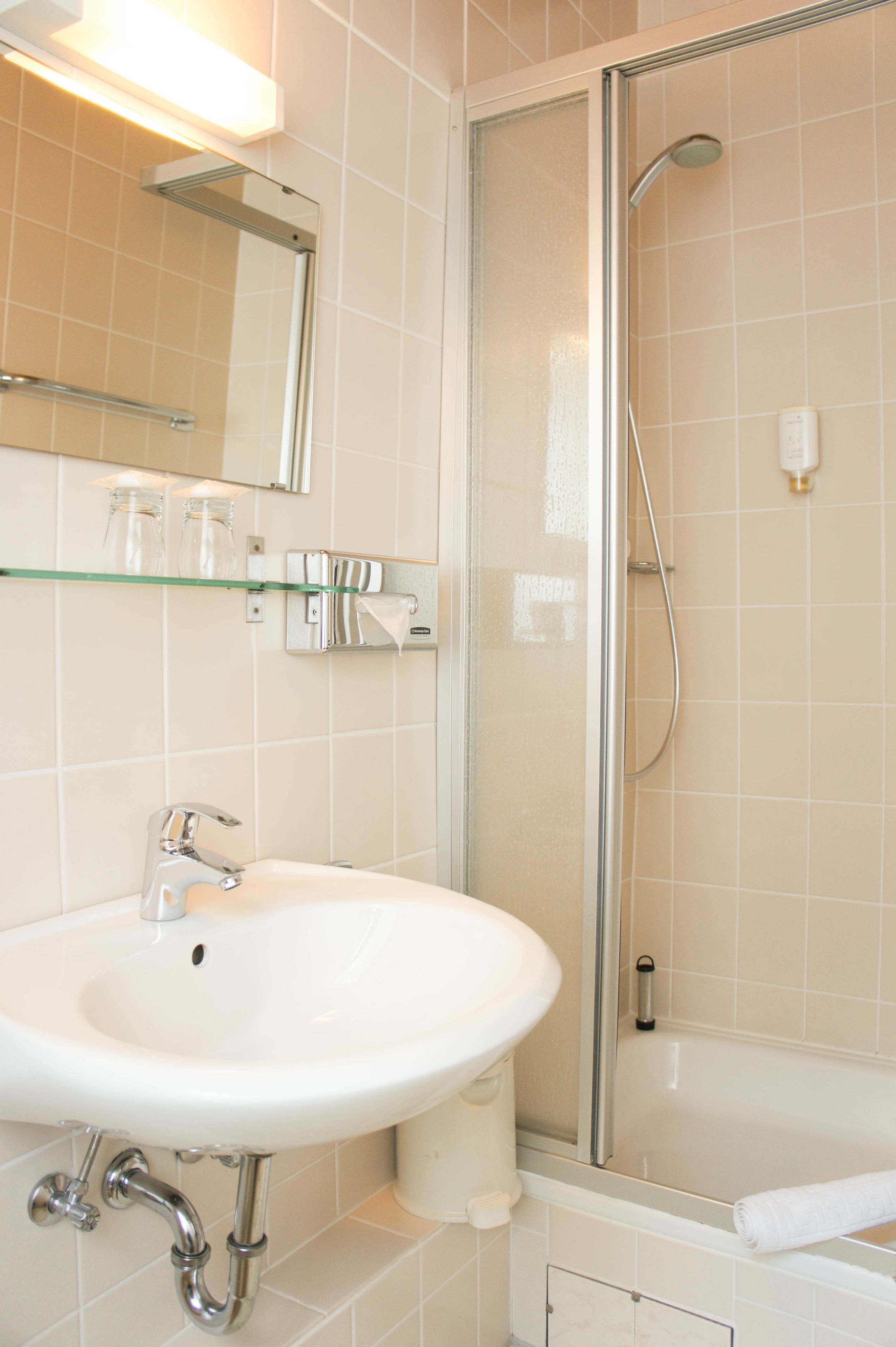 Une salle de bain avec un lavabo blanc, des étagères en verre, un miroir et une douche à parois de verre.