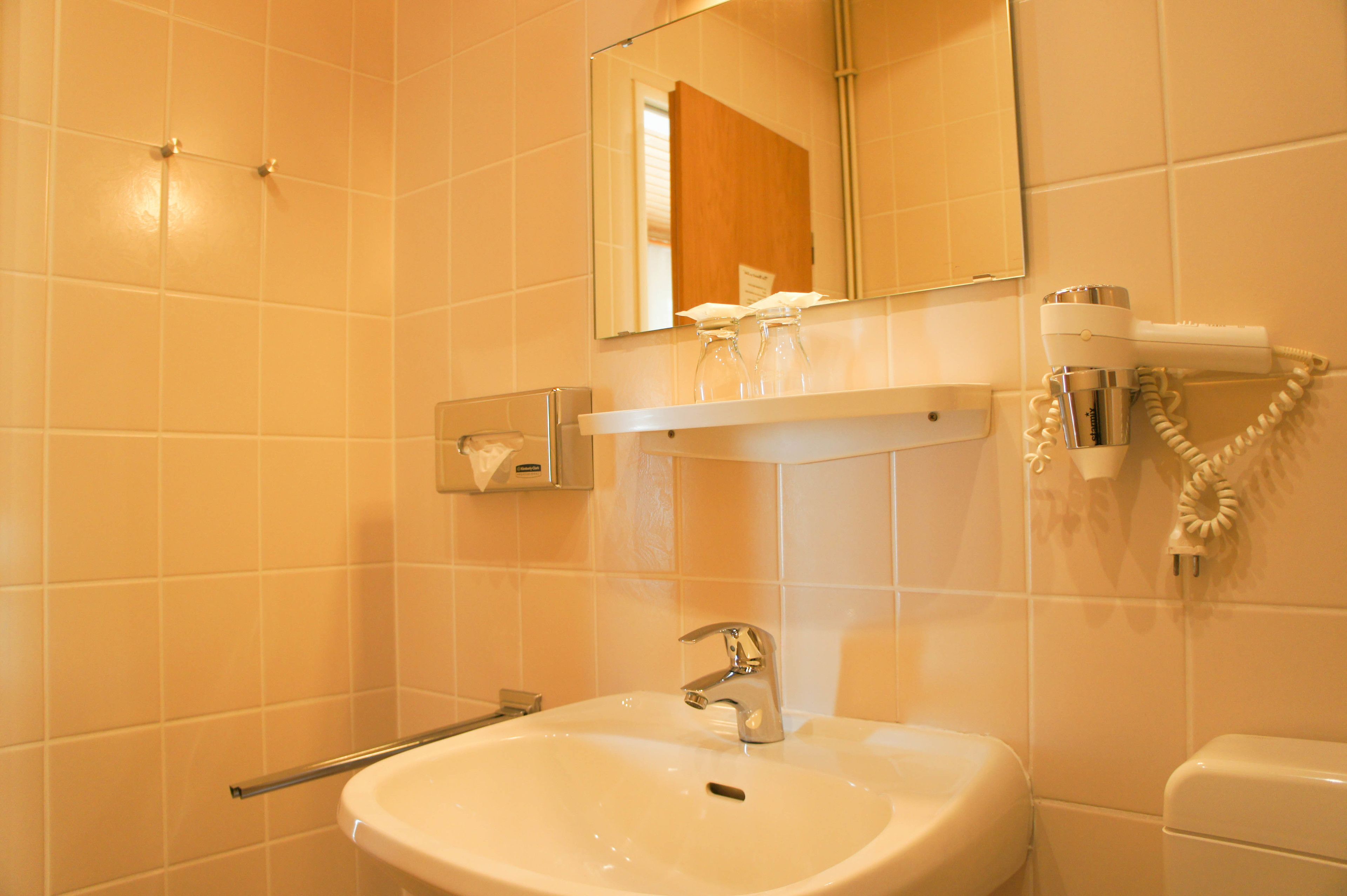 Une salle de bain équipée d’un lavabo, d’un miroir, d’un distributeur de serviettes et d’un sèche-cheveux.