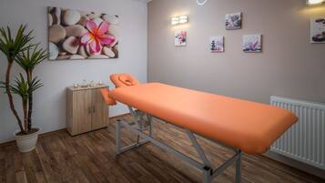 Ein Zimmer mit Holzboden, Massagetisch, Schrank und Wandbildern.