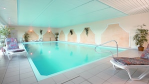 An indoor swimming pool with tiled flooring, white lounge chairs, and potted plants. - AKZENT Hotel Haus Sonnenberg (Schotten)