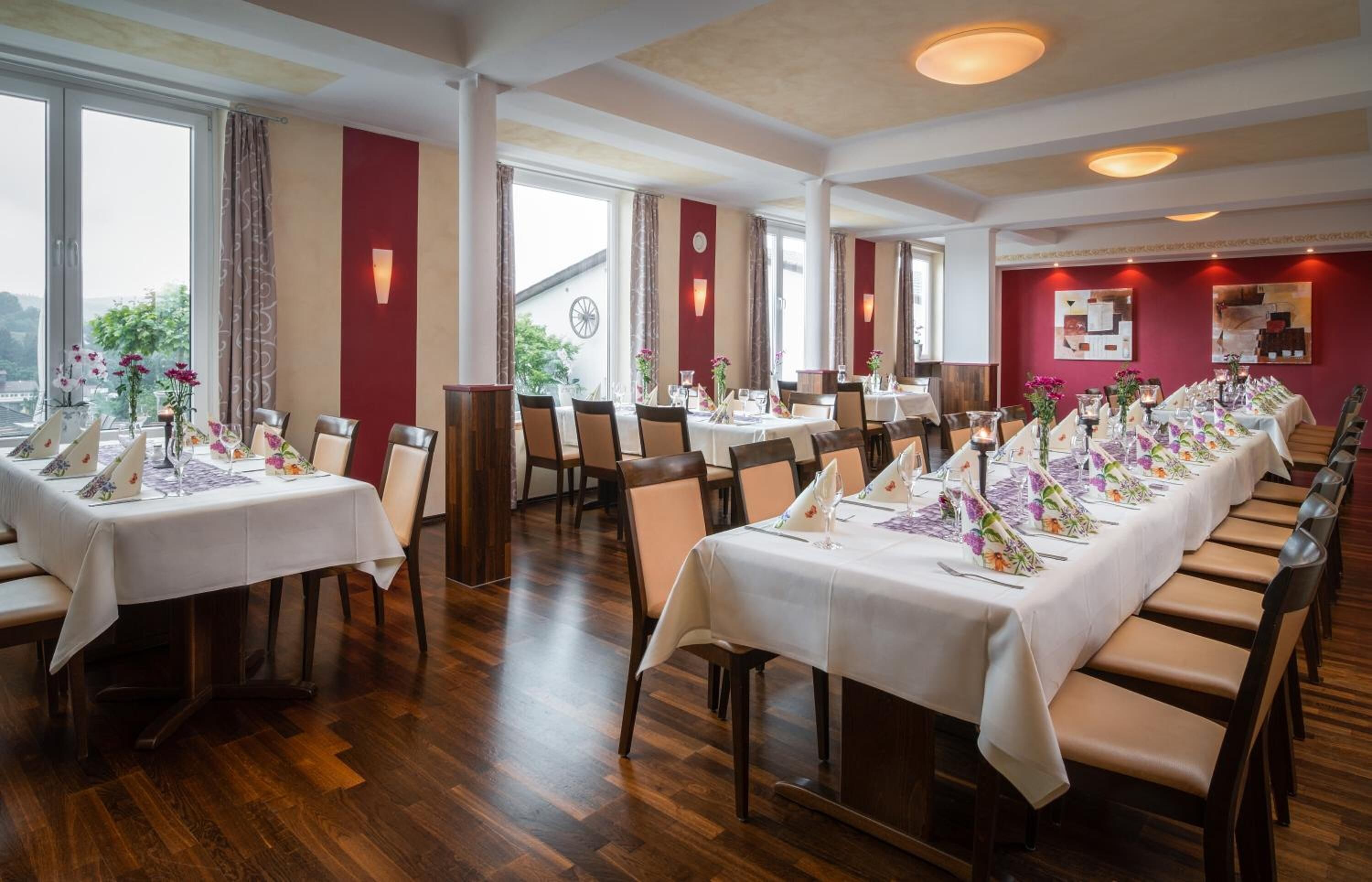 En restaurant med flere borde dækket til spisning, store vinduer og udsigt til det fri.