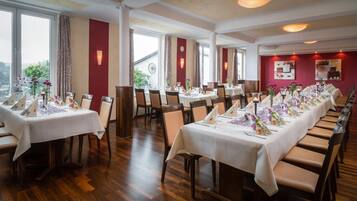 En restaurant med flere borde dækket til spisning, store vinduer og udsigt til det fri.