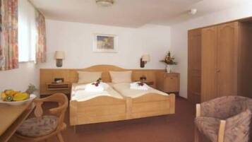 A hotel room with a wooden bed, two bedside tables, a chair, a desk with a fruit bowl, and a wardrobe.