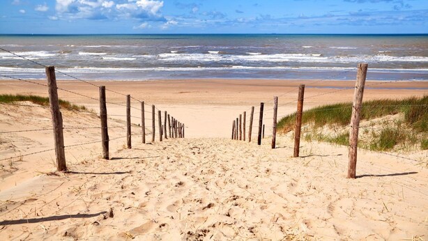 A sandy beach with a wooden fence leading to the ocean. - Hotel Astoria (Noordwijk)